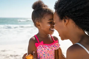 Mother applying sunblock to child's face, avoiding sunscreen in the eyes