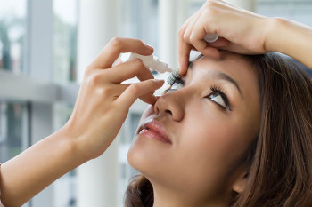 A woman puts drops in her eyes.