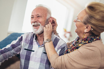 A wife adjusts her husband's hearing aids