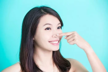 A woman points to her nose after getting a rhinoplasty