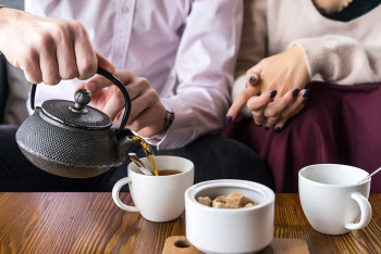 A man and woman drink tea to soothe their dry throats.