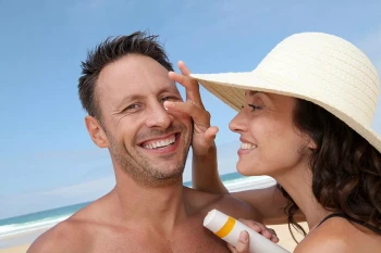 A woman applies sunscreen to a man's face. She avoids sunscreen in his eyes