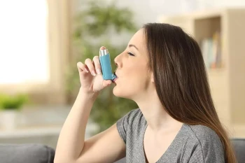 A woman uses an inhaler to treat asthma, which may be caused by her allergies.