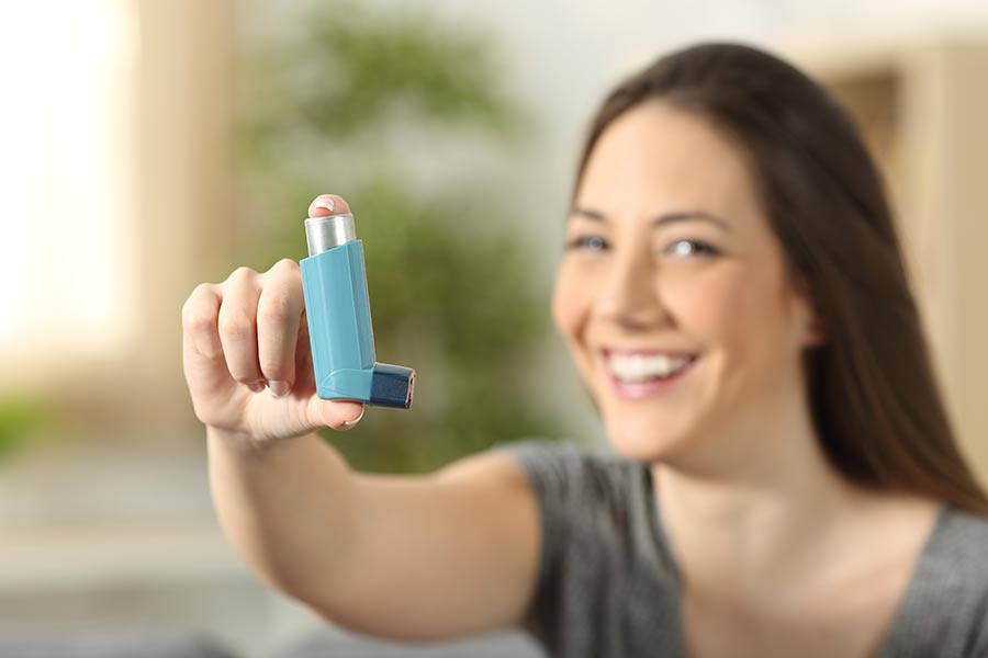 A woman holds up her inhaler, which she uses to treat allergy-related asthma.